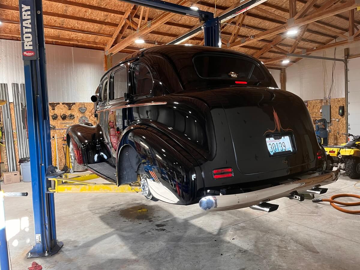 A black car is sitting on a rotary lift in a garage.
