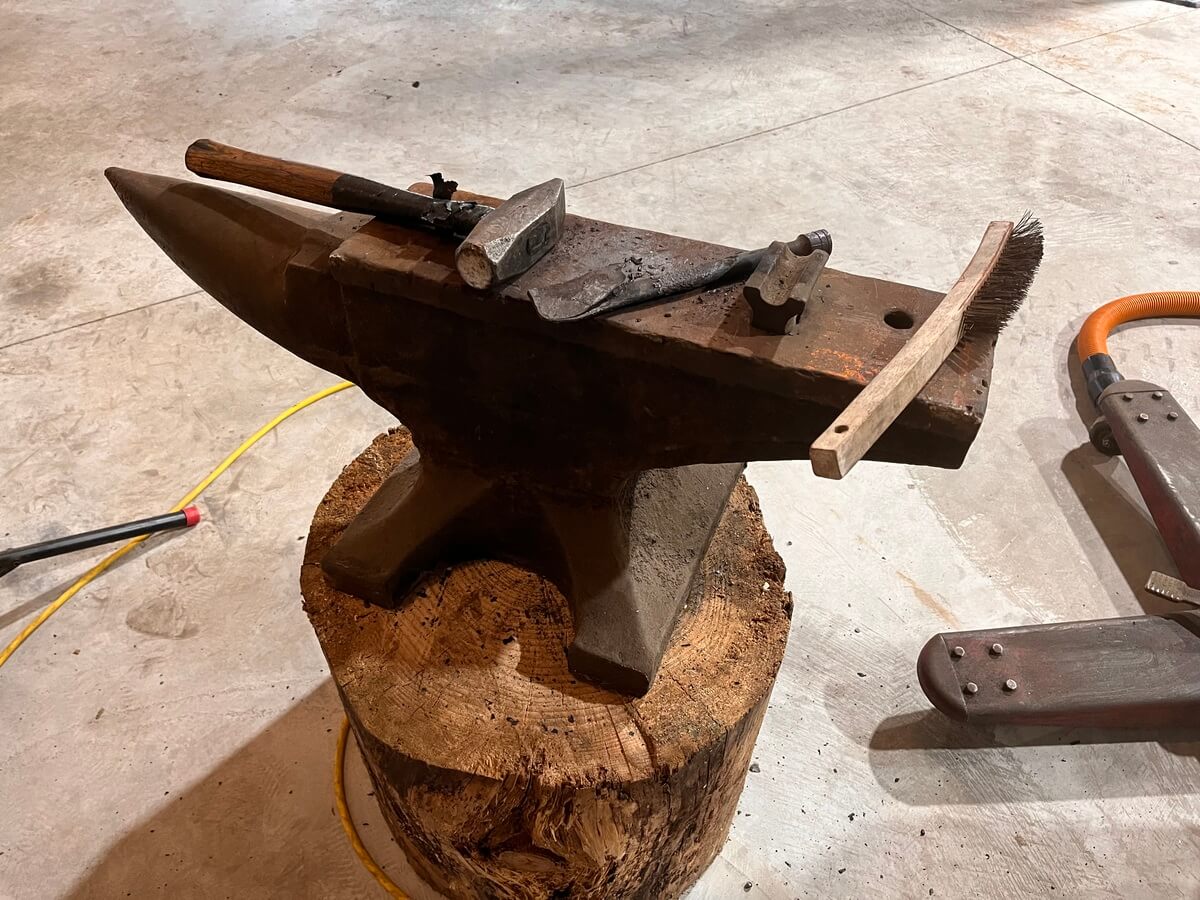 A large anvil is sitting on top of a tree stump.
