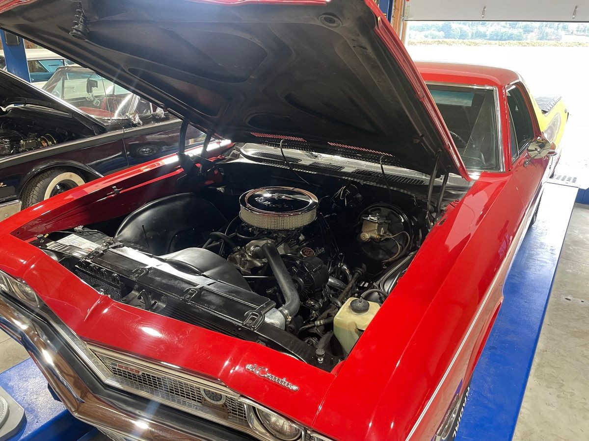 A red car with the hood up is sitting on a lift.