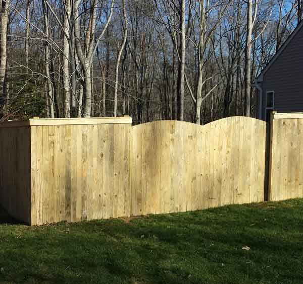 A wooden fence in a backyard with trees in the background.