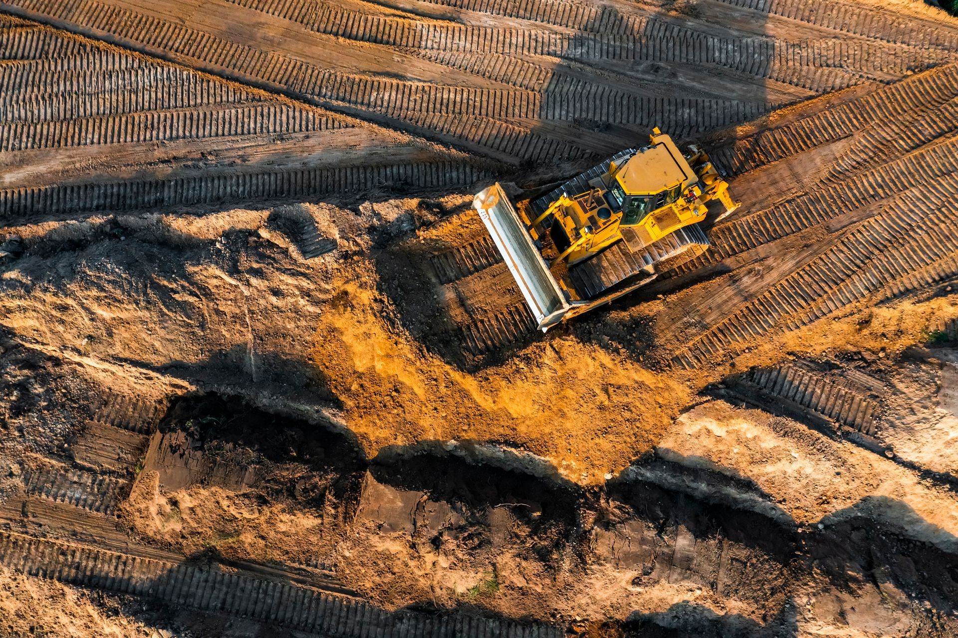 An aerial view of a bulldozer digging a hole in a dirt field.