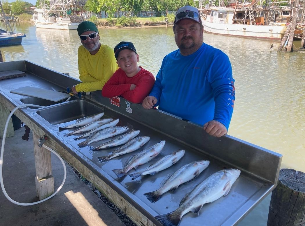 Three men are standing next to a sink filled with fish.
