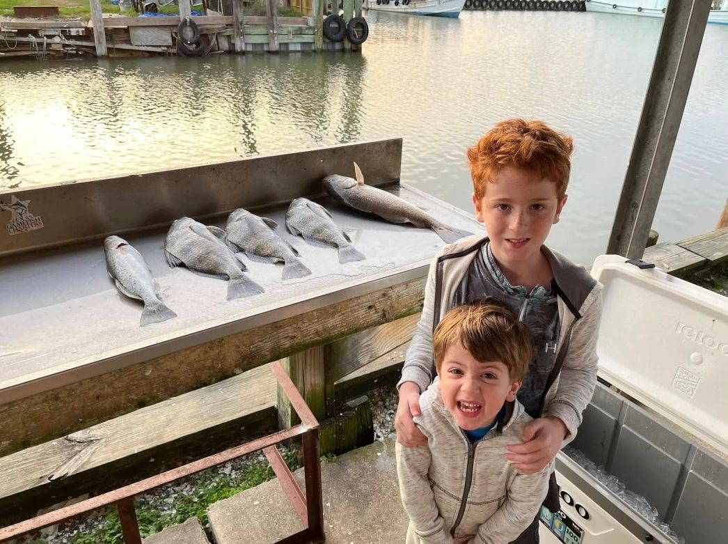 Two young boys are standing next to a table with fish on it.