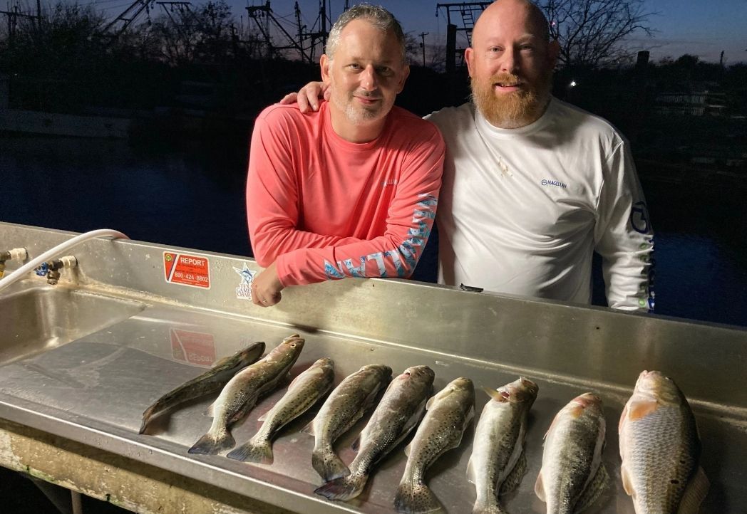 Two men are standing next to a table full of fish.