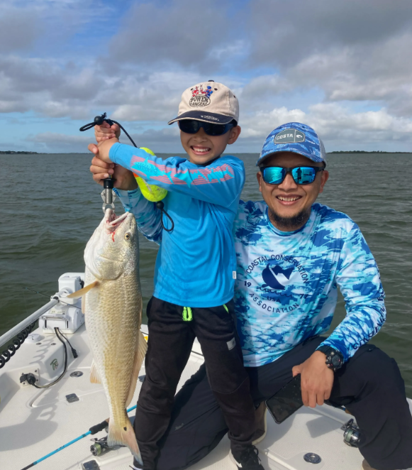 A man and a boy on a boat holding a fish