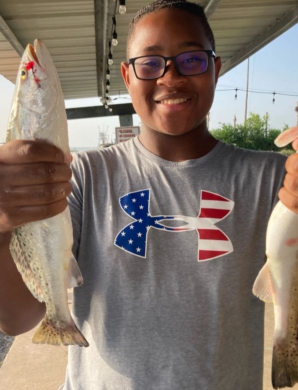 A boy wearing an under armour shirt is holding two fish