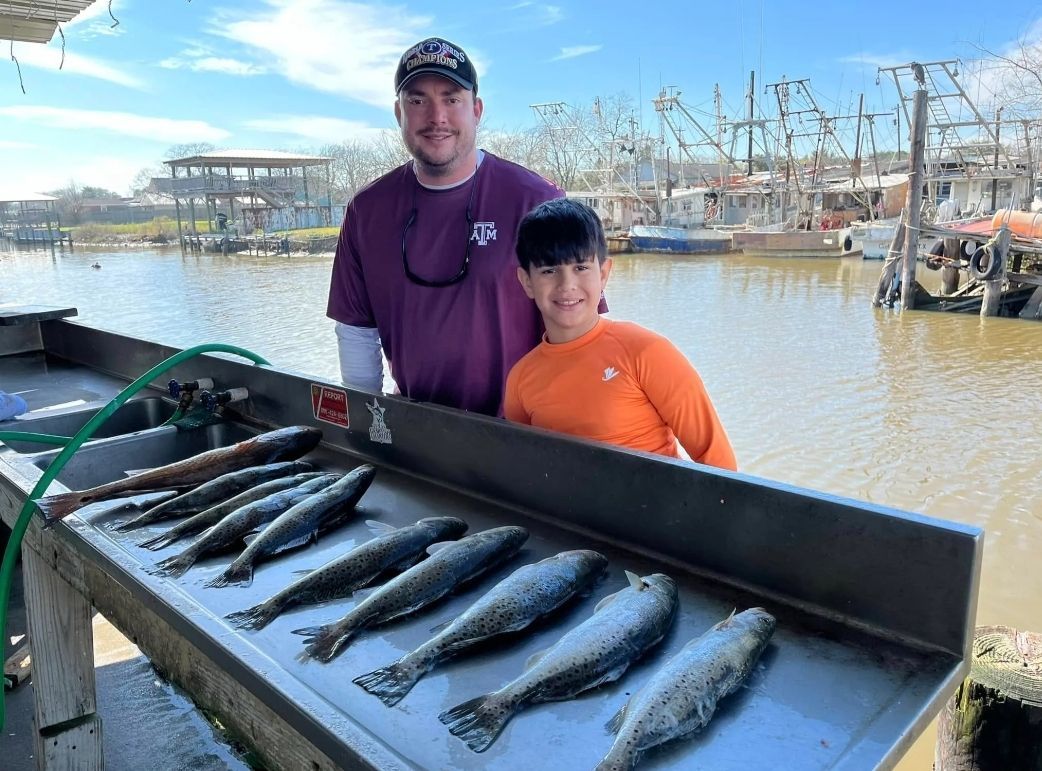 A man and a boy are standing next to a table full of fish.
