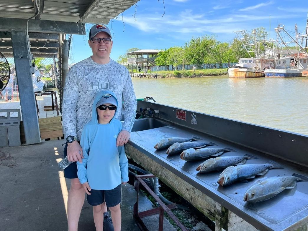 A man and a boy are standing next to a table with fish on it.