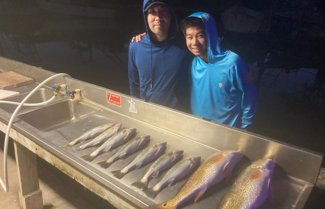 Two men are standing next to a sink filled with fish.