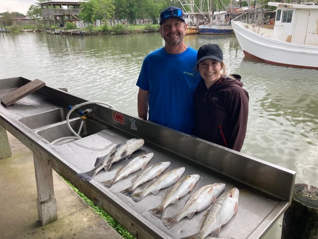 A man and a woman are standing next to a sink filled with fish.