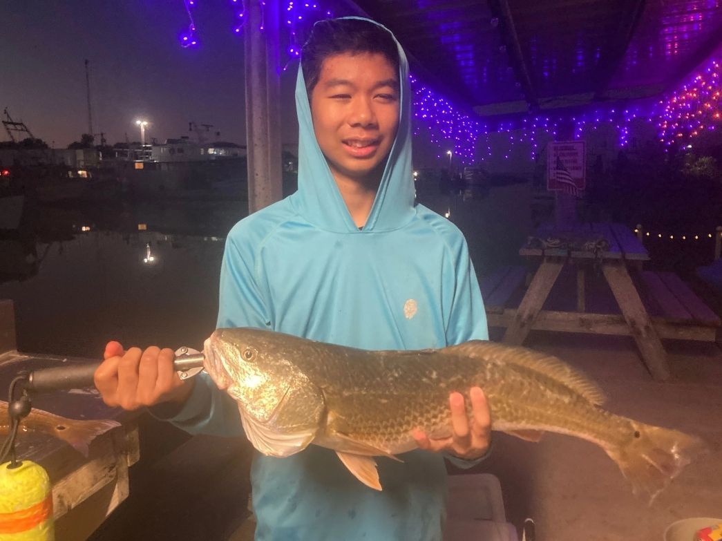 A young boy is holding a large fish in his hands.