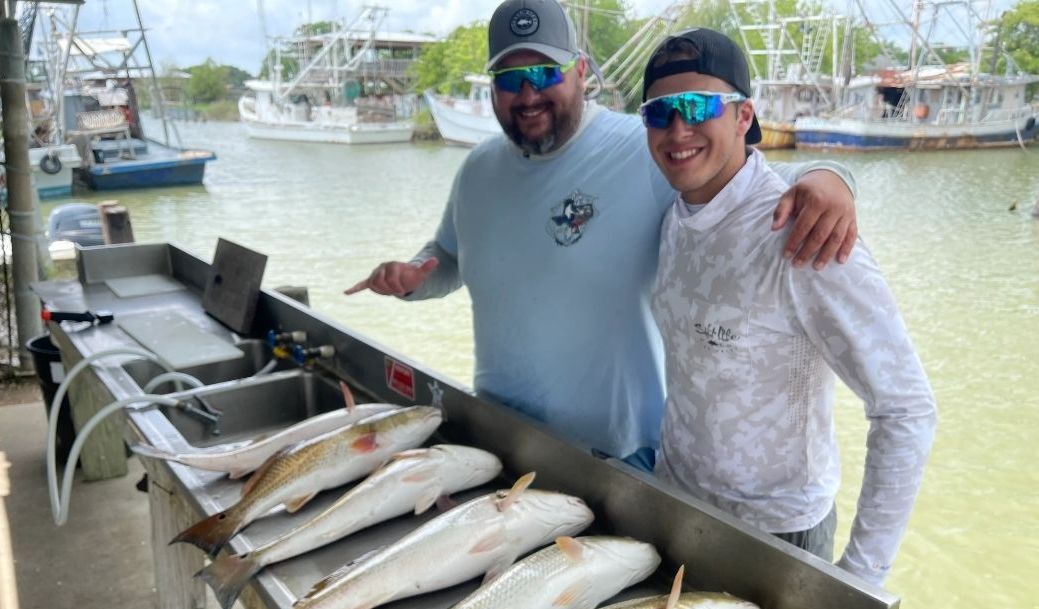 Two men are standing next to a table full of fish.