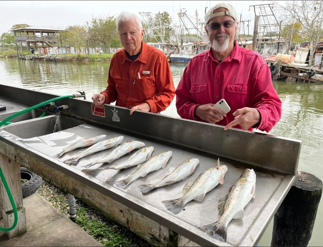 Two men are standing next to a table filled with fish.