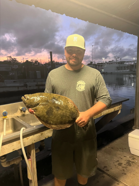 A man is holding a large fish in front of a sink.