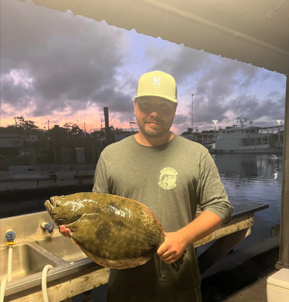 A man in a baseball cap is holding a large fish