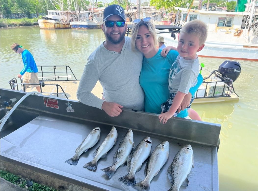 A man , woman and child are standing next to a table with fish on it.