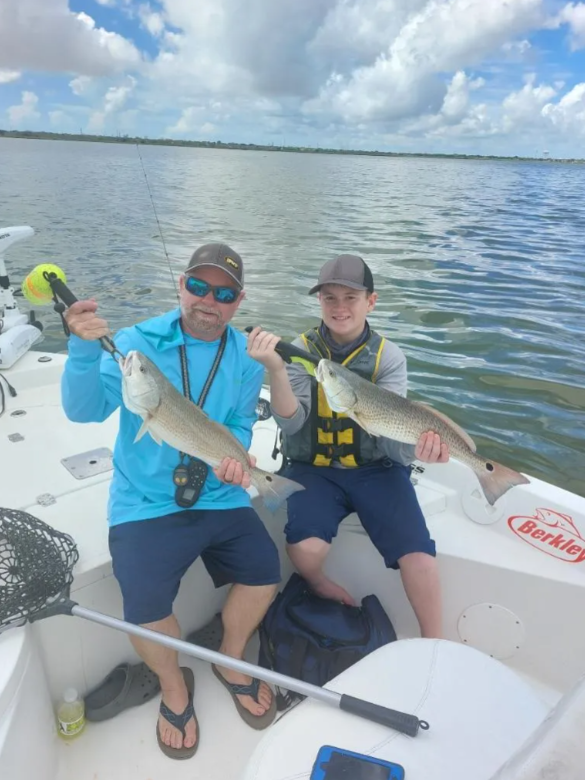 A man and a boy are sitting on a boat holding fish