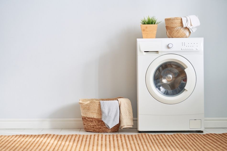 A white washing machine is sitting next to a basket of towels in a laundry room.