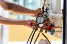 A man is working on an air conditioner with a pressure gauge.