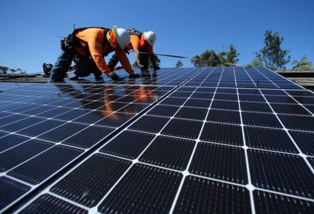 Operai che installano pannelli solari su un tetto sotto un cielo azzurro.
