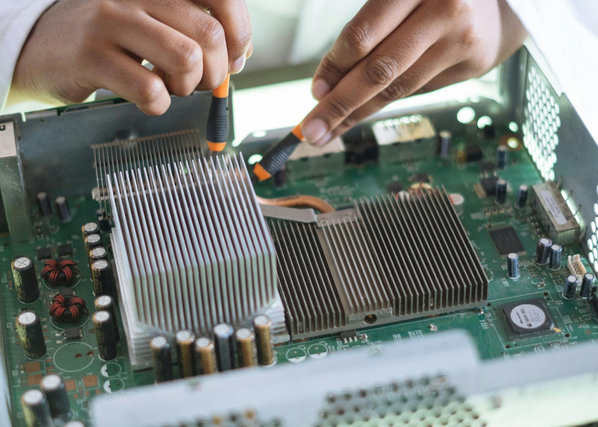 Hands using screwdrivers to repair a circuit board with heat sinks.