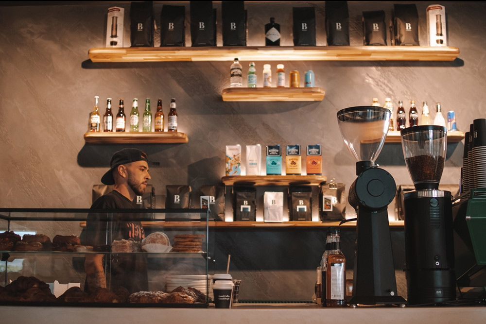 A Man is Standing Behind a Counter in a Coffee Shop — Barber Bros & Co - Southport in Southport, QLD