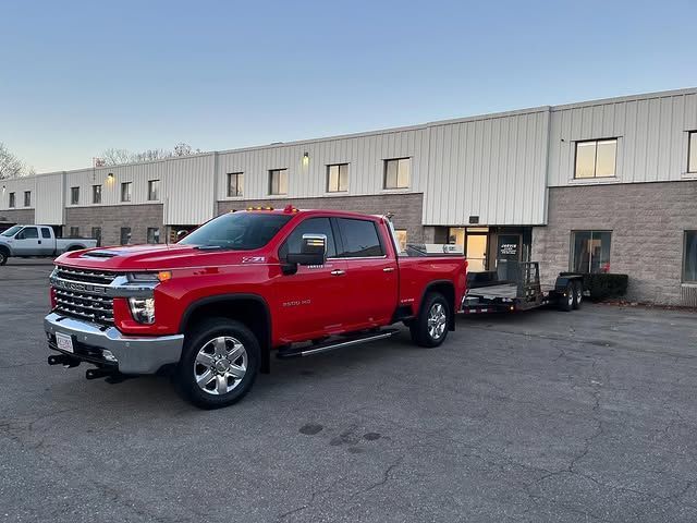 A bright red Chevrolet Silverado pickup truck with an attached flatbed trailer parked in front of a commercial building.