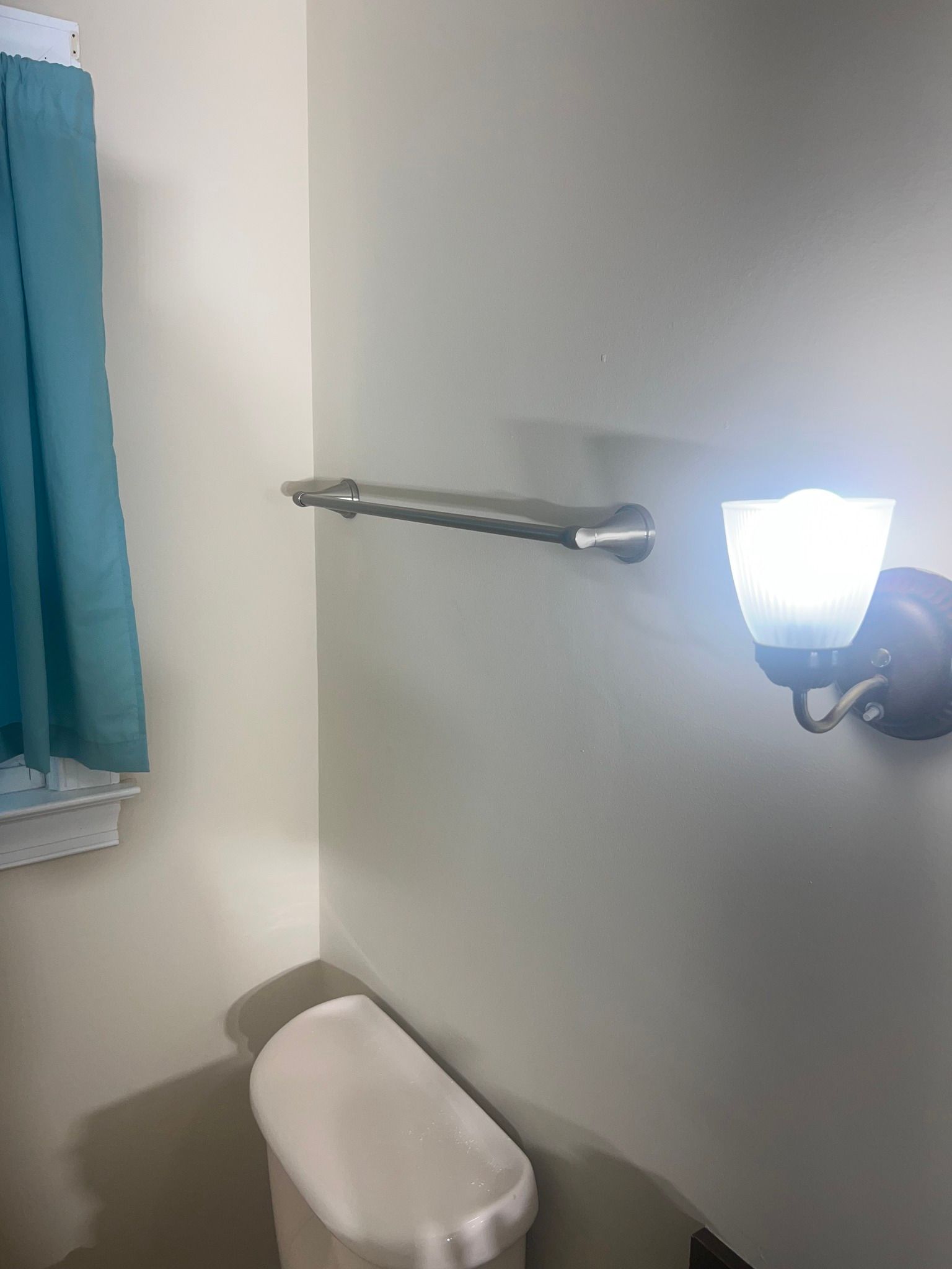 A bathroom with a toilet , towel rack , and light.