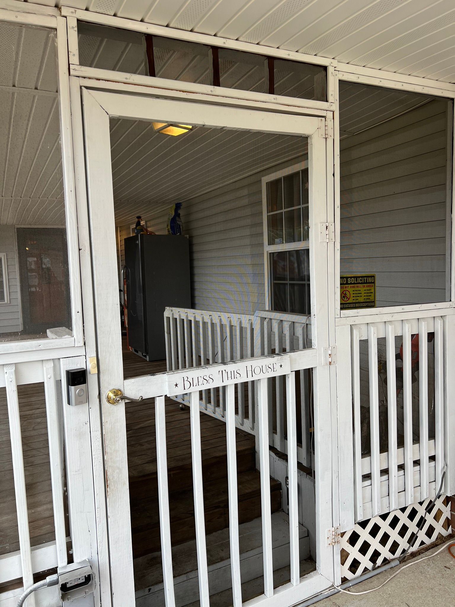 A screened in porch with a broken screen door and stairs leading up to it.