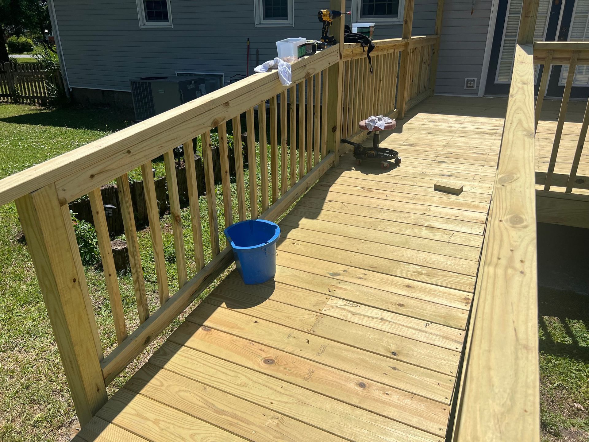 A wooden deck with a blue bucket on it in front of a house.