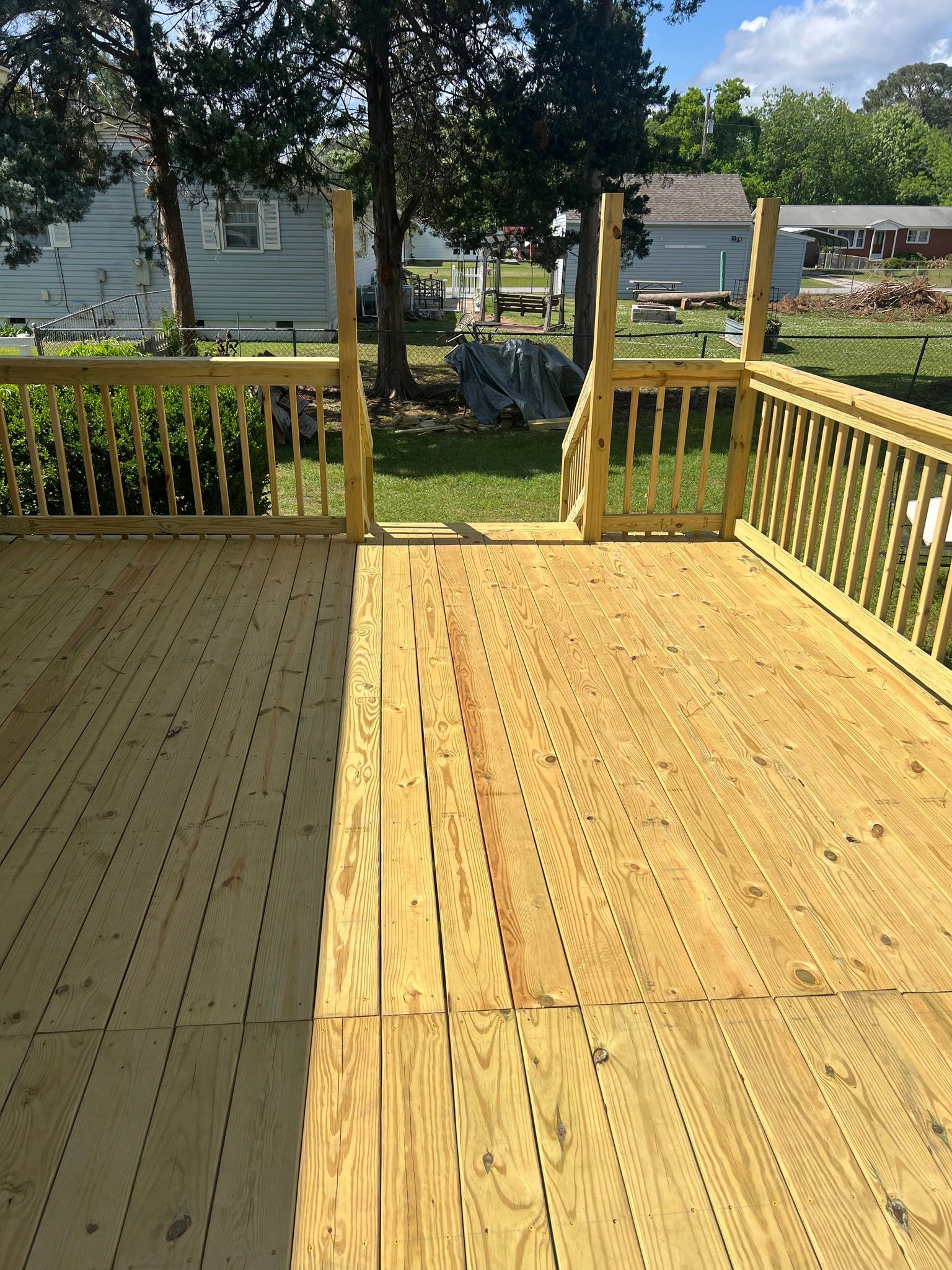 A wooden deck with a railing and a house in the background.