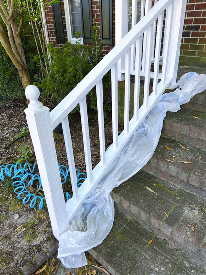 White painted staircase railing, partially covered with plastic sheeting. A blue hose lies nearby.