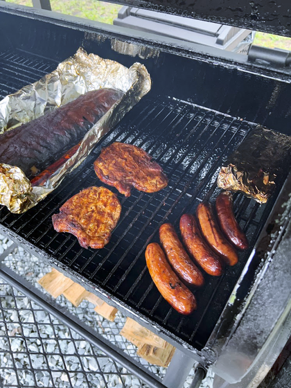 Smoked meats on a barbecue grill: ribs in foil, pork chops, and sausages.