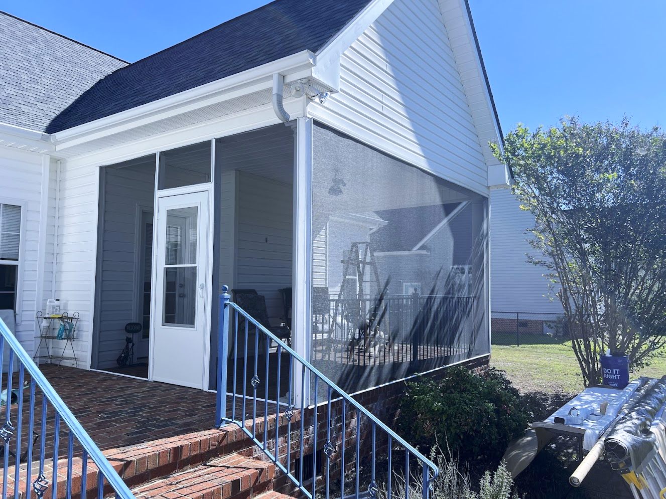A white screened porch with a brick staircase. The porch has a white door, black screens, and a dark roof.