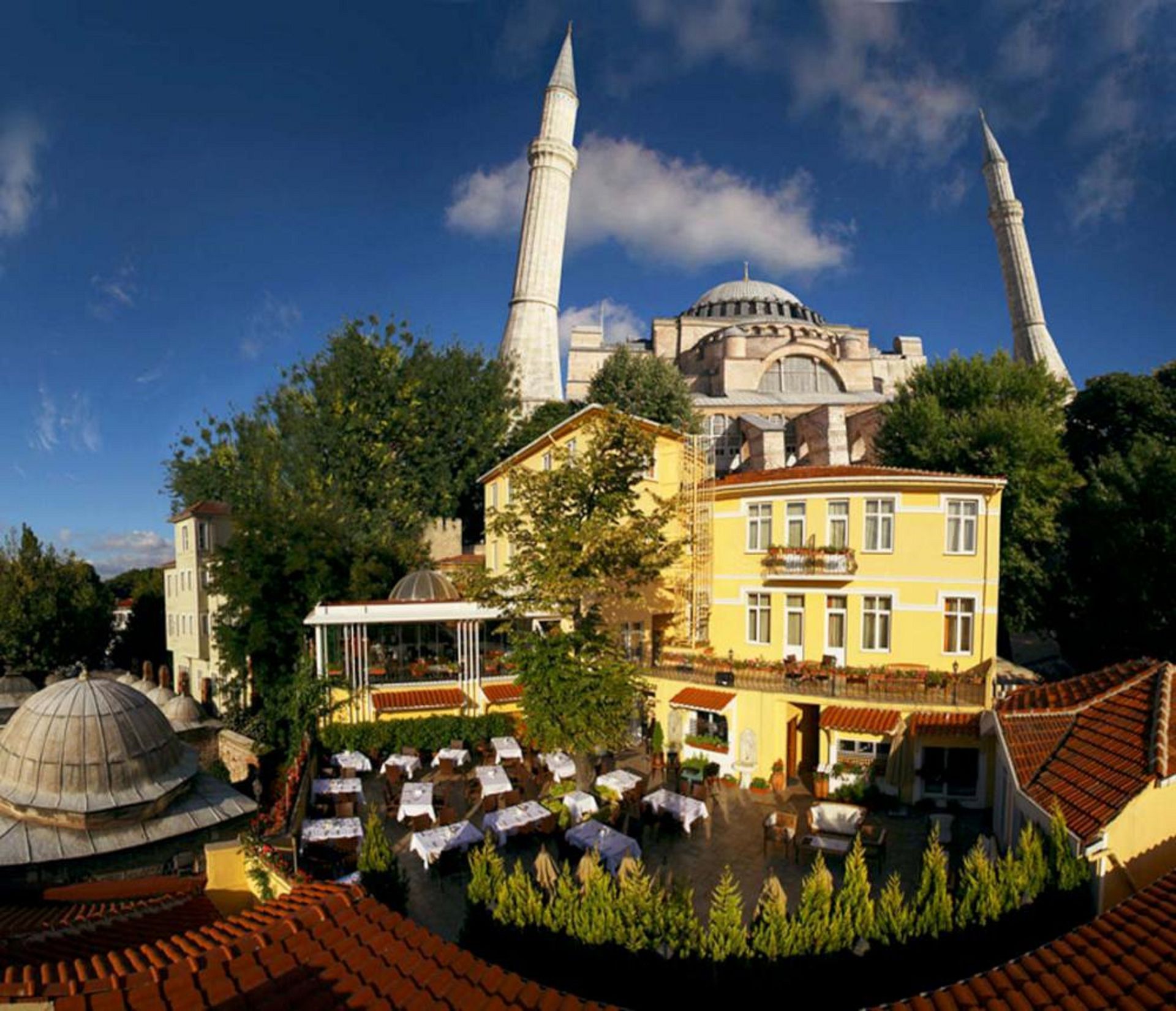 Rooftop restaurant with tables set. Hagia Sophia mosque with minarets in the background, blue sky.