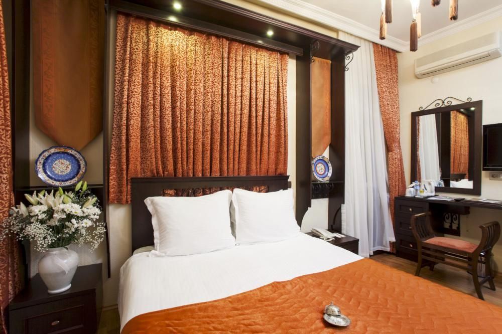 Bedroom with an orange bedspread, curtains, and a dark wood frame around the window and bed.