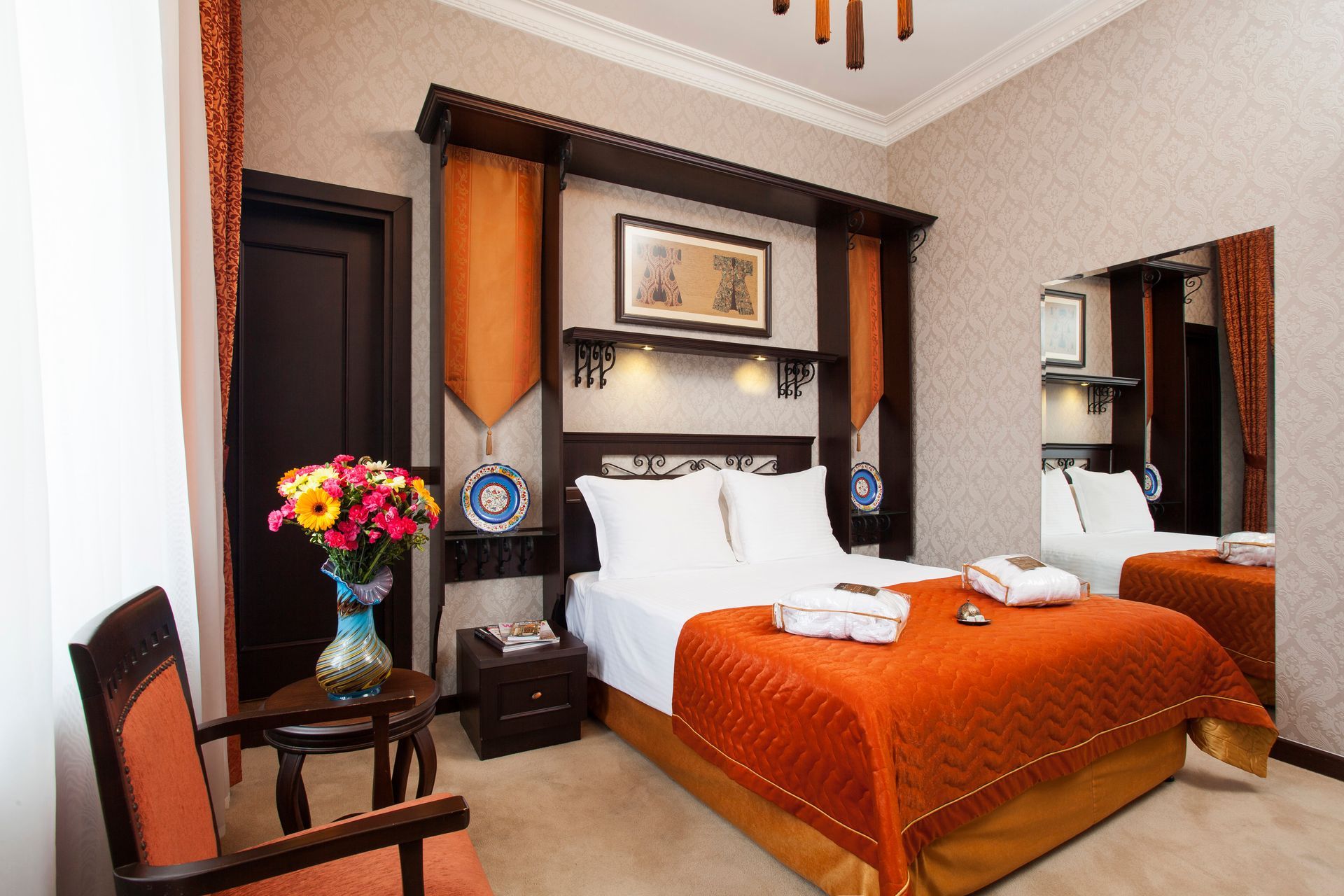 Hotel bedroom with double bed, orange bedding, dark wood accents, and a large mirror.