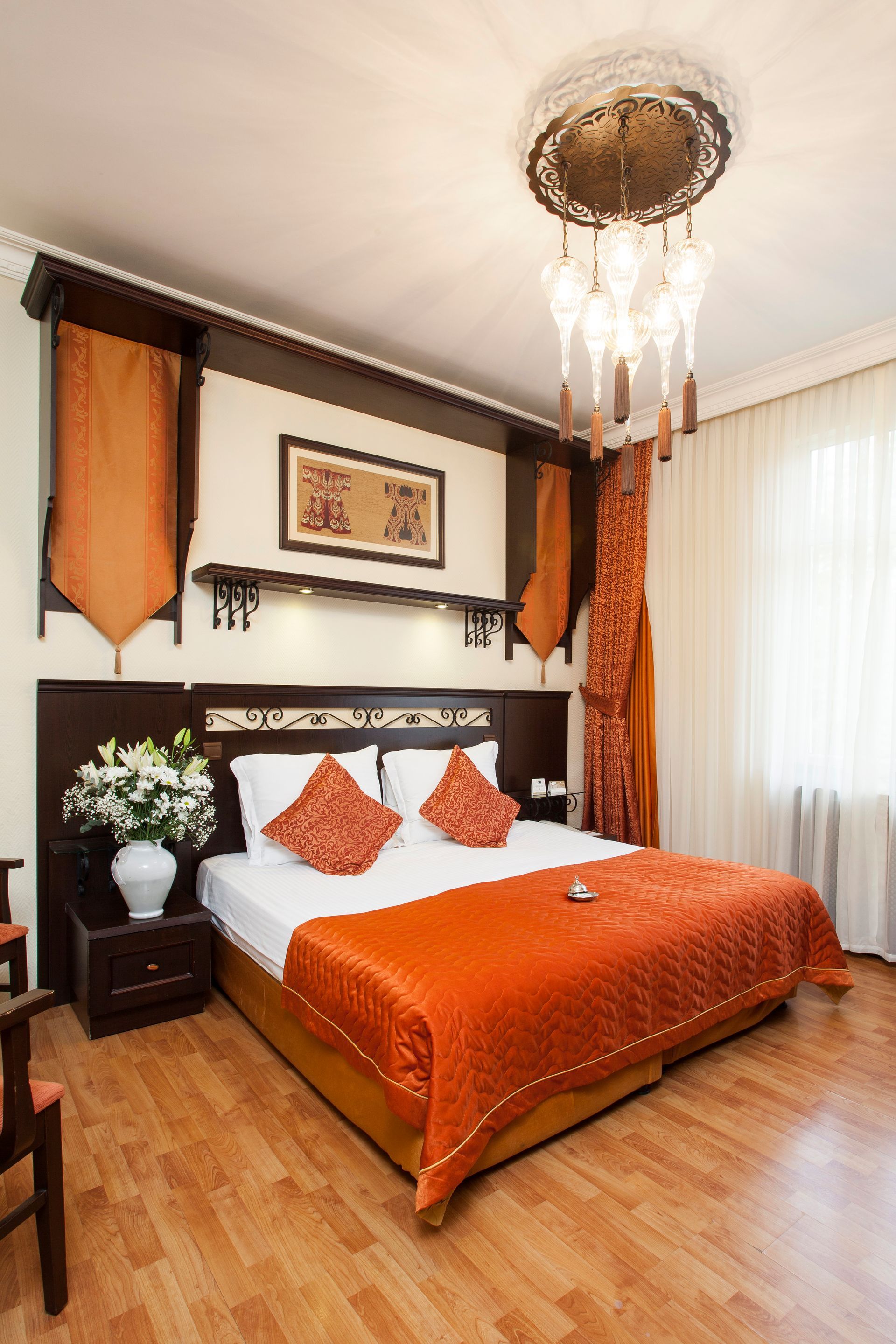 Hotel bedroom with a bed, nightstand, and orange accents; decorative chandelier.