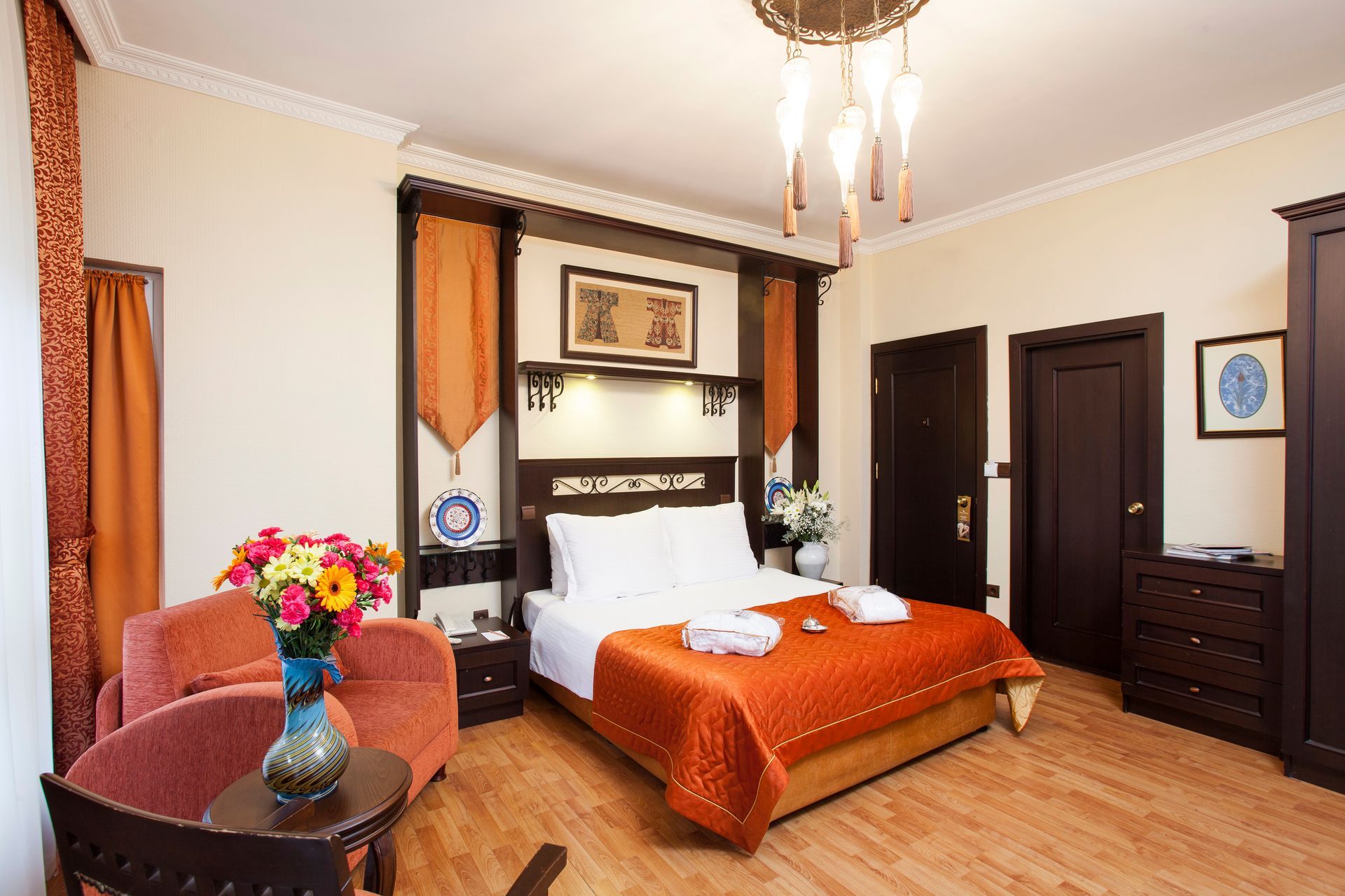 Hotel room with bed, chair, and wooden furniture; orange and brown tones.