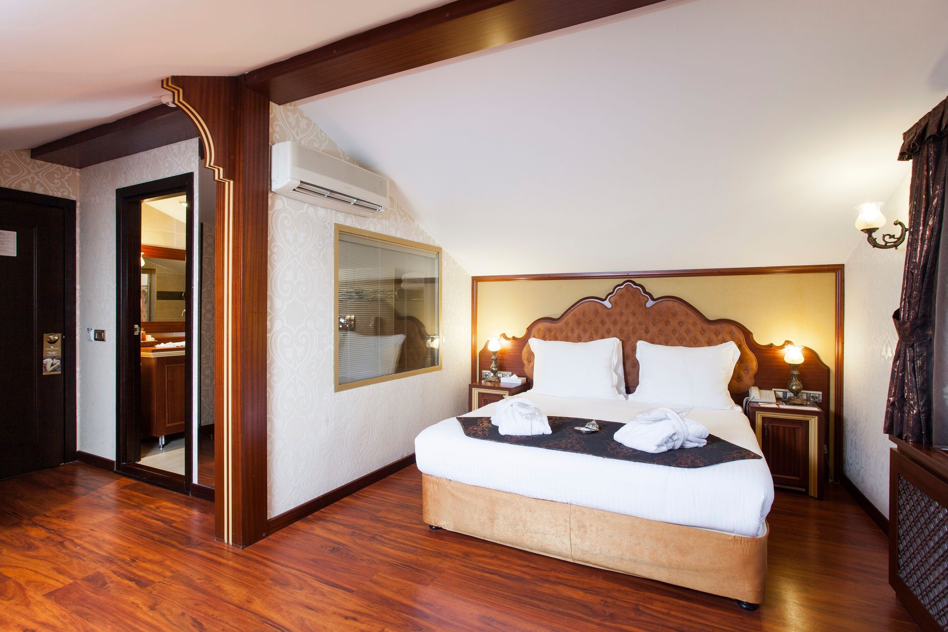 Hotel bedroom with a bed, wood floor, and a bathroom visible through a doorway.