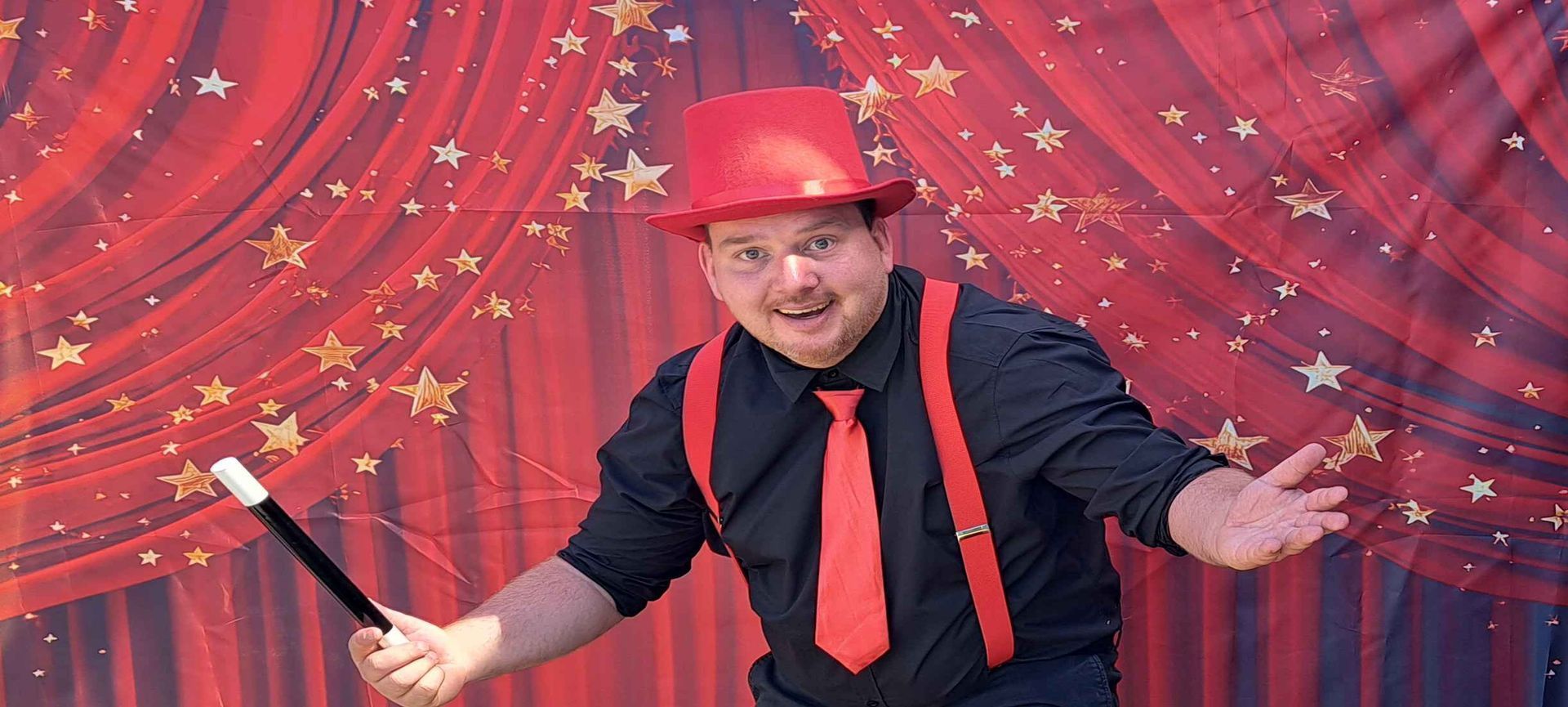 Een man met een rode hoed en stropdas houdt een toverstaf vast voor een rood gordijn.