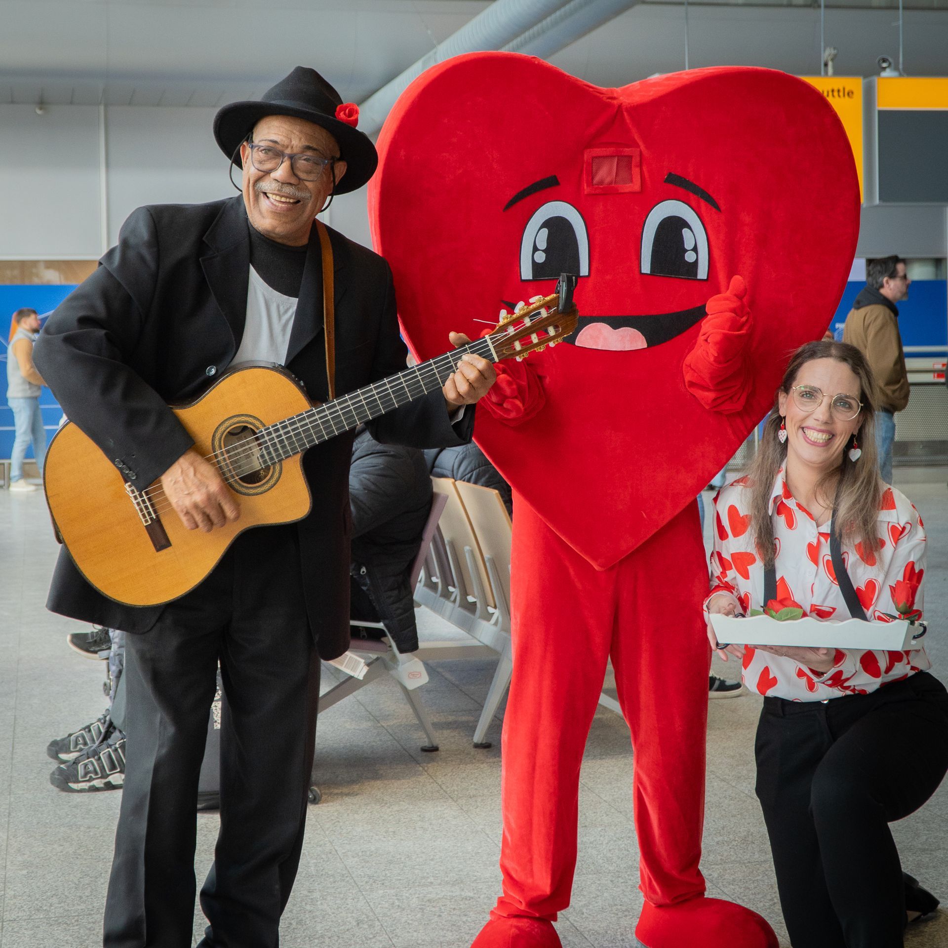 Een man die gitaar speelt naast een mascotte met een rood hart