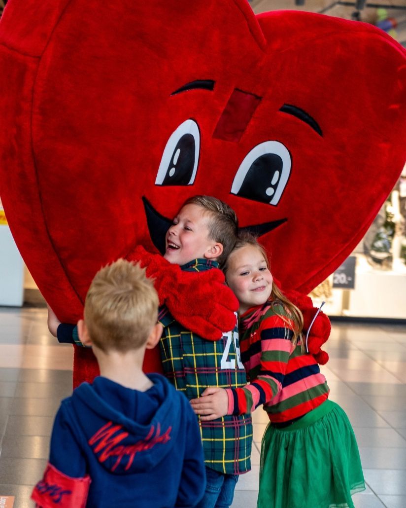 Drie kinderen omhelzen een mascotte in de vorm van een hart