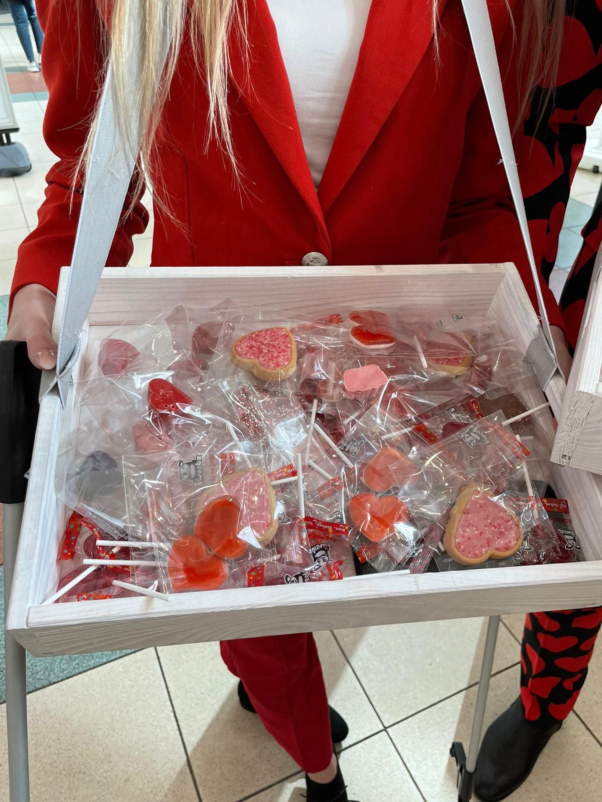 Een vrouw in een rood pak houdt een dienblad met hartvormige lolly's vast