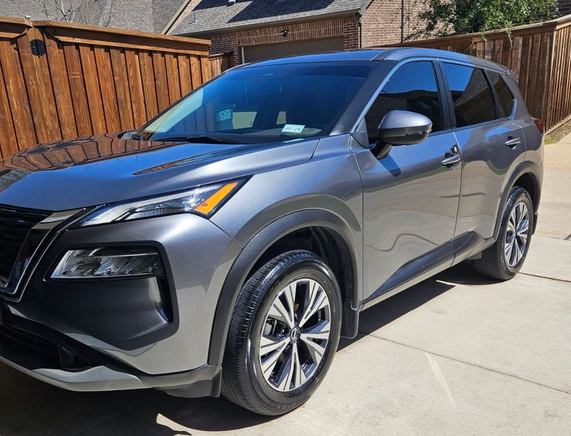 A nissan rogue is parked in a driveway next to a wooden fence.
