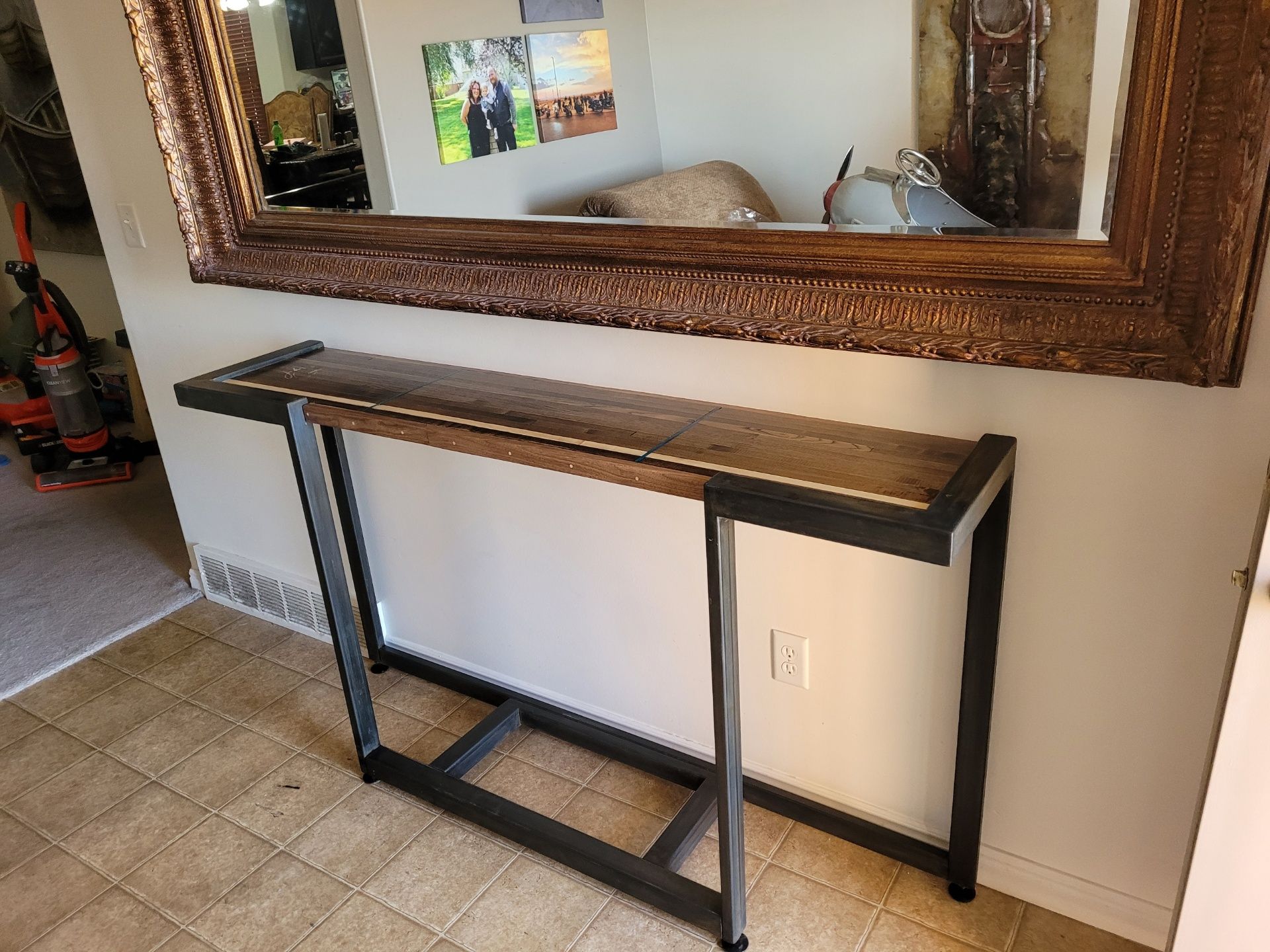 A console table with a wooden top and metal frame beneath a large framed mirror.
