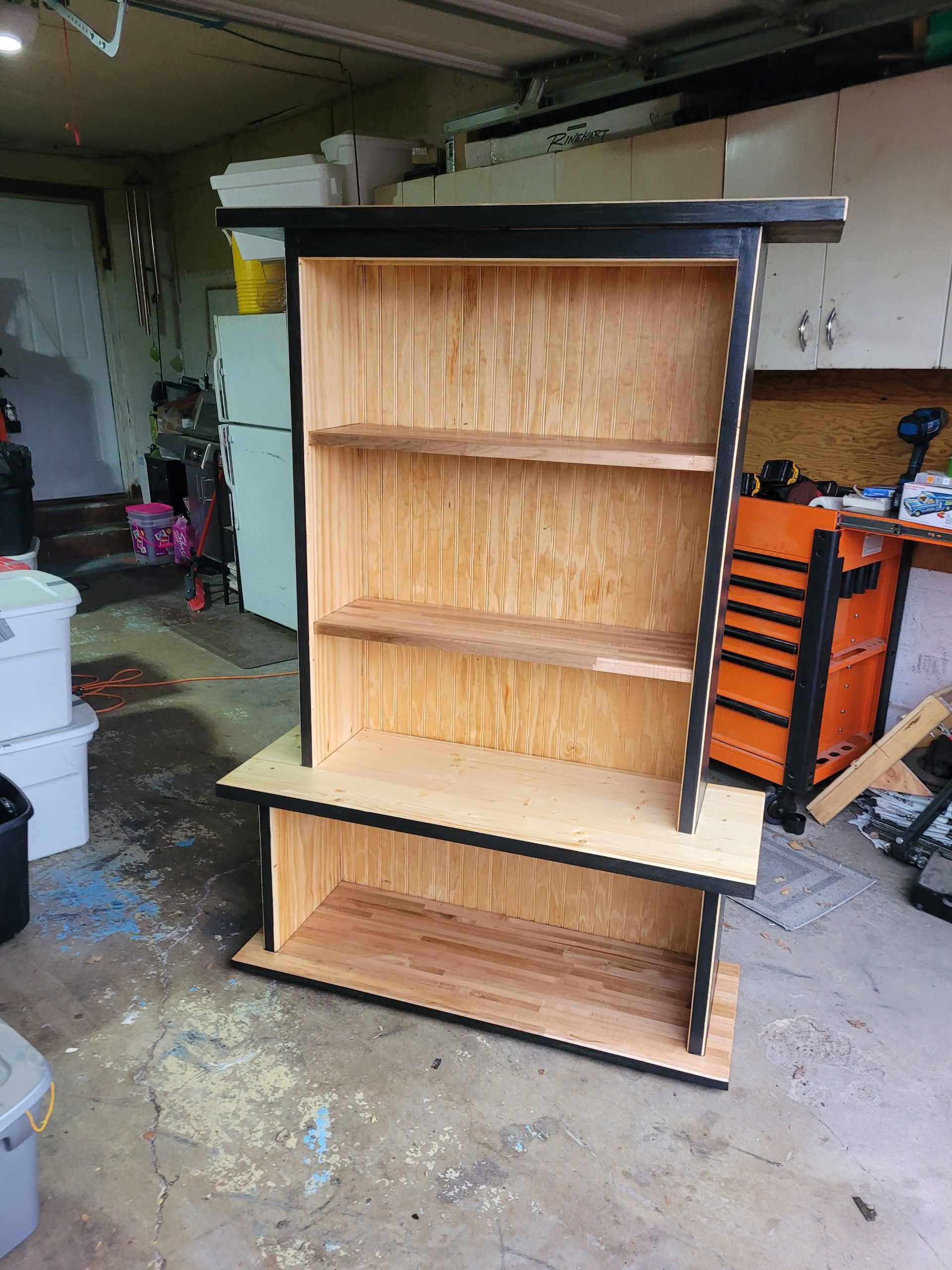 Two-tiered wooden bookshelf with black trim, in a garage setting.