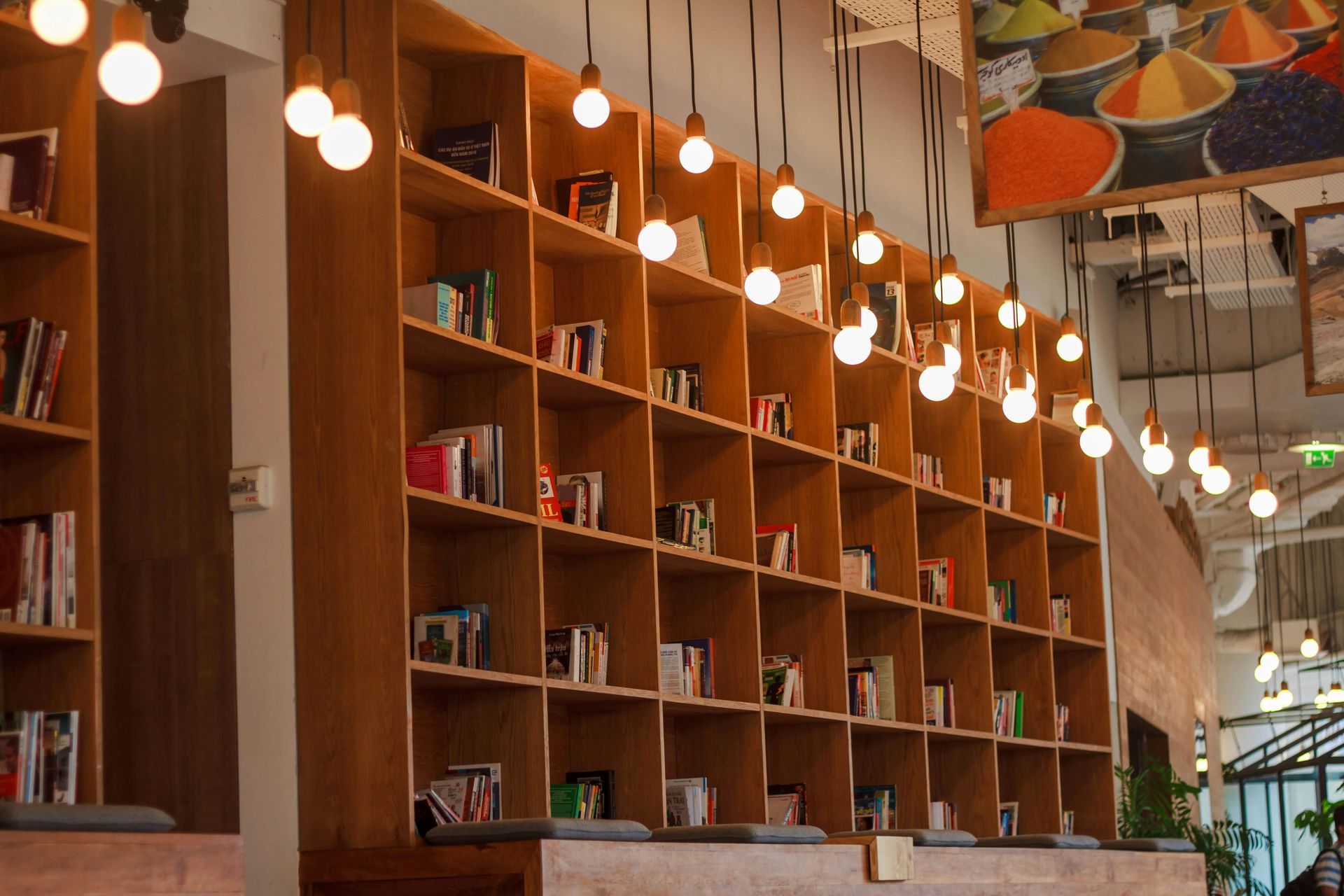 Wooden bookshelves filled with books, lit by hanging lightbulbs in a cafe or library.