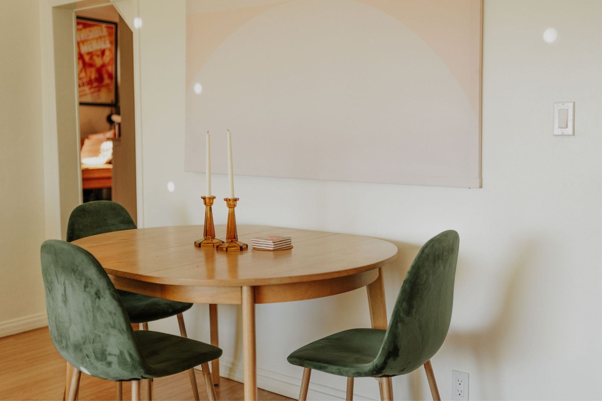 Dining room with wooden table, green velvet chairs, and a pink abstract painting.