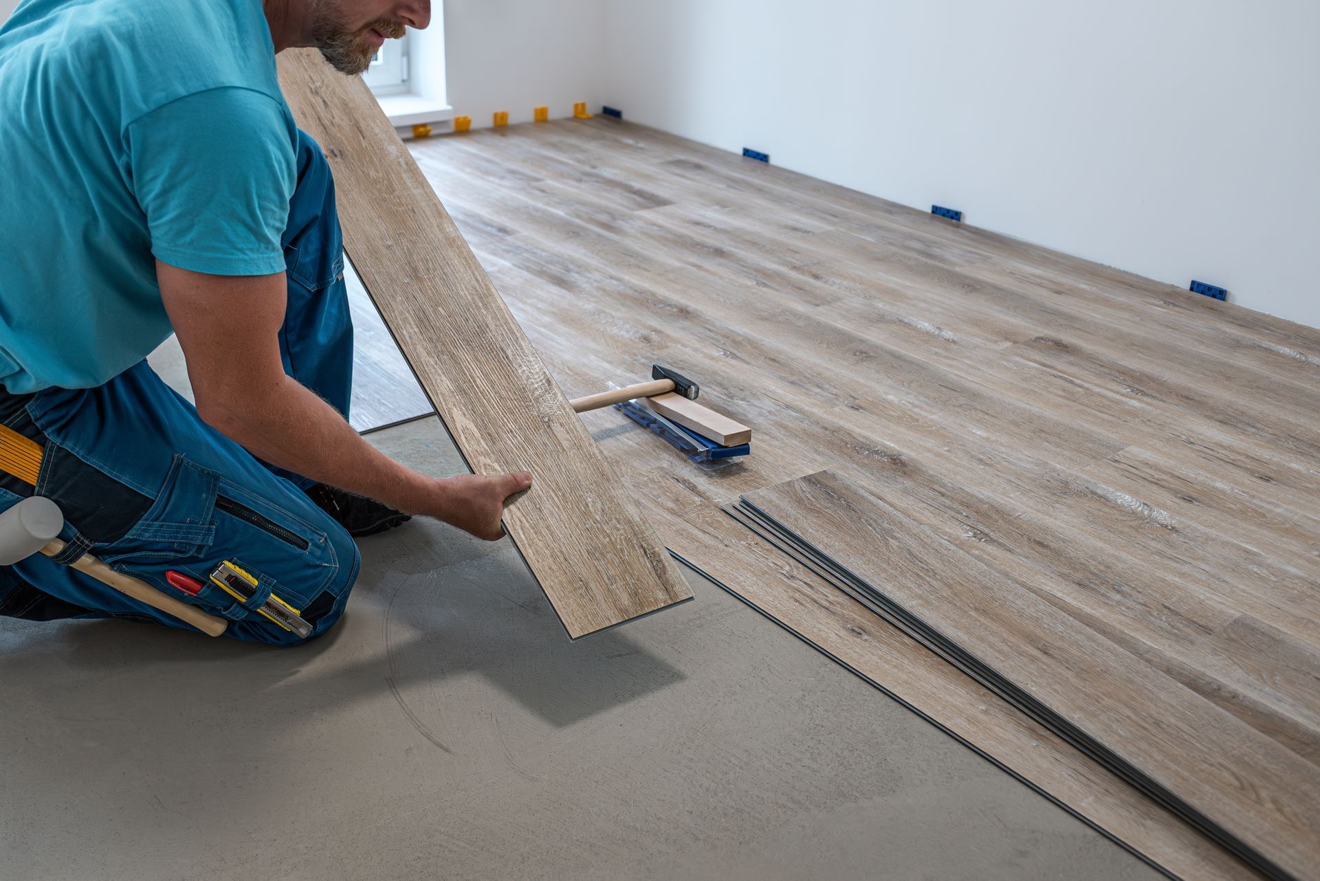 Man installing wood-look flooring. Kneeling in room, placing a plank, tools nearby.